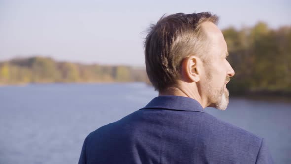 A Middleaged Handsome Caucasian Man Looks Around Over a River on a Bridge in a Park in Fall