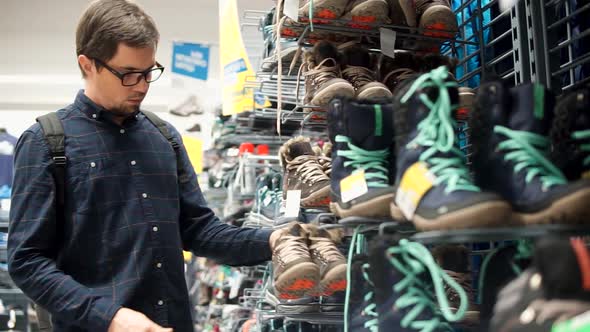 Man is Watching with Astonishment on a Pair of Male Shoes for Walking in a Shop alt