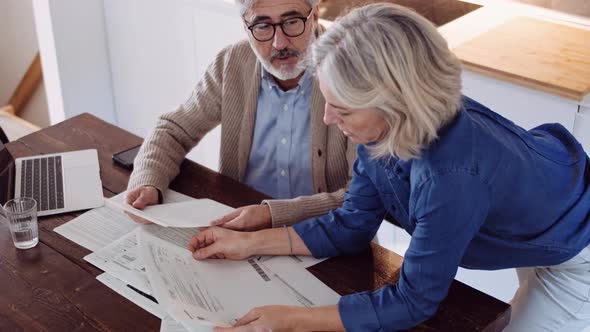 Slow motion shot of mature couple with papers and laptop on table alt