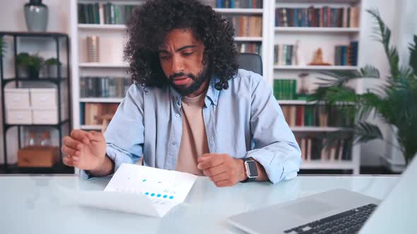 Puzzled Young Arabian Man Entrepreneur Examines Paper Financial Audit alt