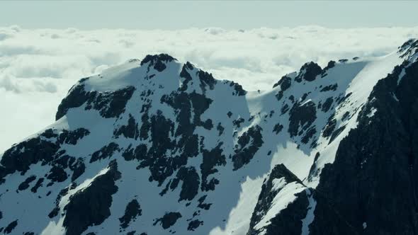 Aerial Tracking Shot of a close Mountain Range Peaking through High Altitude White Clouds