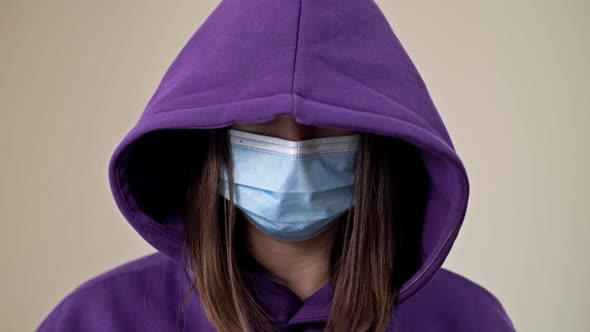Woman in a Hood and a Medical Mask Demonstrates a Gesture Indicating the Need for Help alt