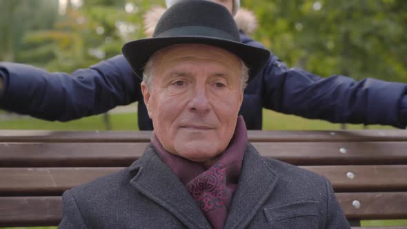 Cheerful Caucasian Girl Coming From the Background and Closing Eyes of a Mature Man in Elegant alt