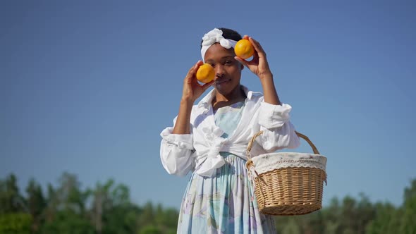 Charming Smiling African American Young Woman Posing Outdoors with Vitamin Oranges alt