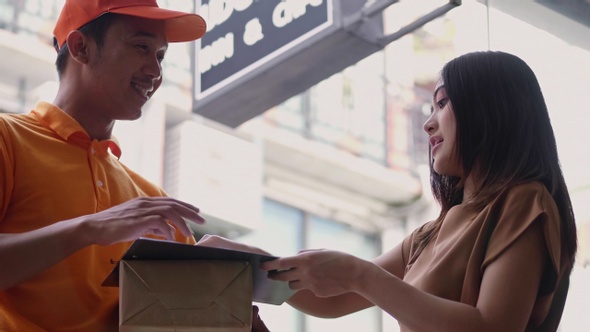 Delivery man holding a cardboard box while Asian young woman putting signature in the clipboard.