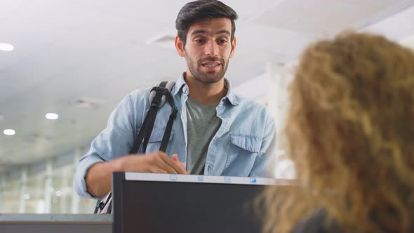 Caucasian male passenger handing phone to airline staff for scanning at check in counter in airport alt