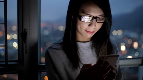 Woman wearing glasses and working on mobile phone at night alt