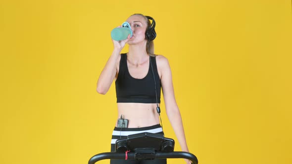 Fit blonde girl in sportswear with headphones works out on a treadmill