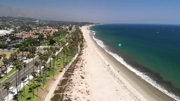 Aerial shot over the palm trees and blue pacific ocean with a kite boarder on the sandy beaches of S alt
