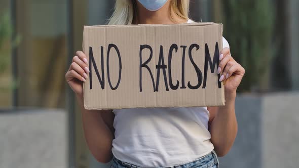 NO RACISM on a Cardboard Poster in the Hands of Female Protester Activist. Closeup of Poster and alt