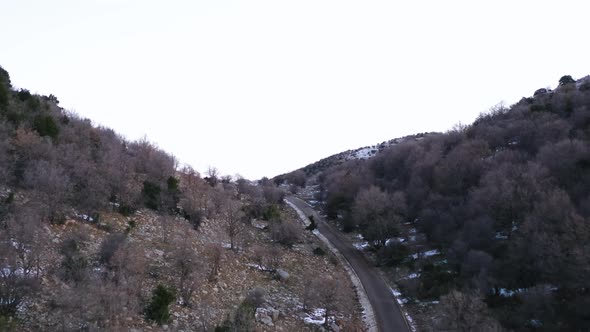 Flying over a high mountain road with light snow on the ground to a panoramic view over a green vall alt
