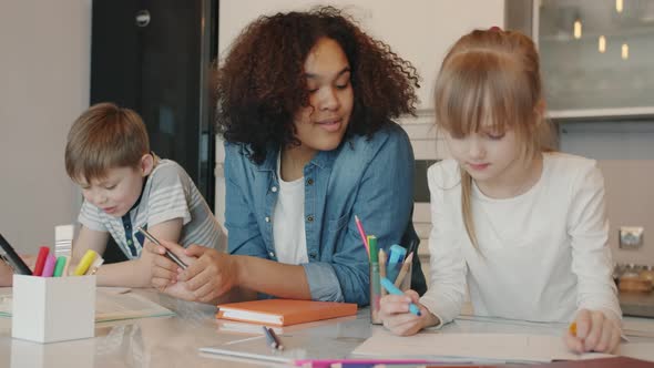 Helpful Babysitter Talking To Kids Doing Homework Writing and Drawing at Home alt