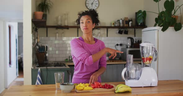 Portrait of mixed race female vlogger making fruit juice in the kitchen at home alt