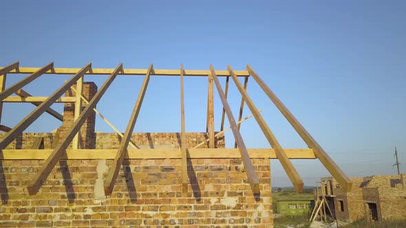 Aerial view of unfinished brick house with wooden roof structure under construction. alt
