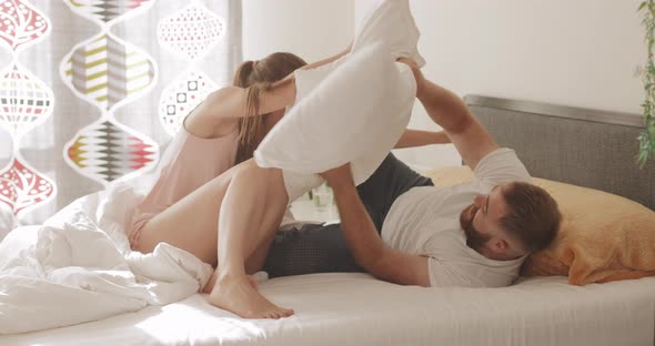 Romantic Couple Fighting with Pillows and Enjoing Time Together in Bedroom. Happy Boyfriend and alt