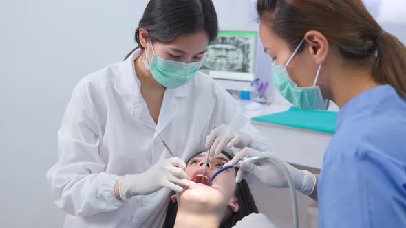 Asian female dentist using an explorer to examining young girl patient's teeth at dental clinic. alt