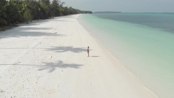 Aerial: Woman relaxing on white sand beach turquoise water tropical coastline alt