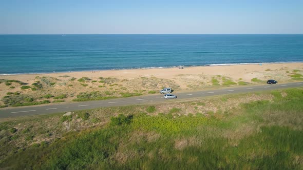 Panoramic View of Cars Driving Slowly on Sea Road with Sand Beach and Calm Sea Horizon with Blue Sky alt