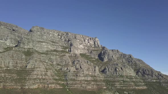 Aerial lower angle scenic drone flight view of Table Mountain in late afternoon sun against blue sky alt