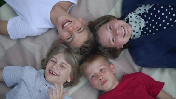 High Angle View Portrait of Relaxed Joyful Children Laughing Looking at Camera Lying on Blanket in alt