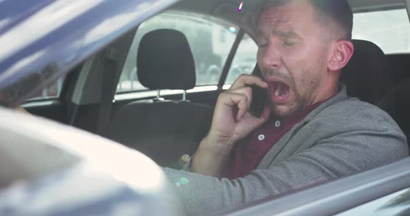 Man Speaking on the Phone at Car Seat Sneezing and Wipes His Nose with a Napkin alt
