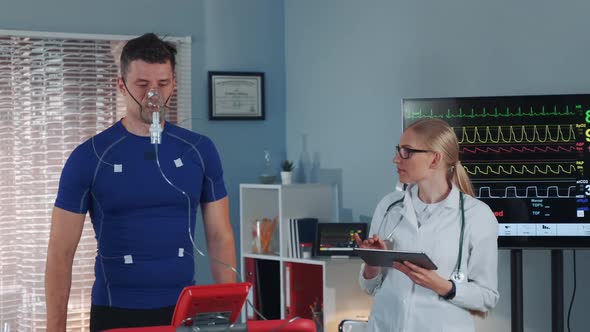 Athlete in Oxygen Mask Doing Stress Test While Cardiologist with Tablet Monitoring His EKG on alt