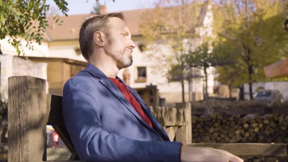 A Middleaged Handsome Caucasian Man Looks Around As He Sits on a Bench in a Quaint Town in Fall