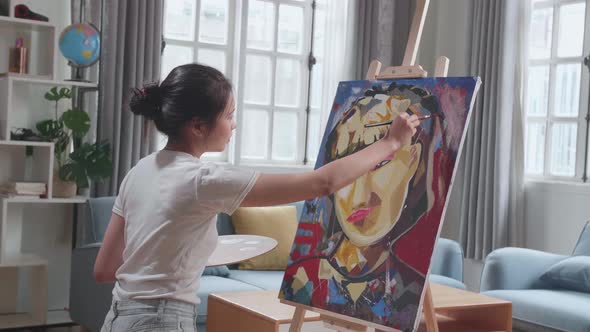 Side View Of An Asian Artist Girl Holding Paintbrush Mixed Colour And Painting On The Canvas alt