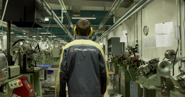 A man in a gray-yellow uniform walks through the production hall_17