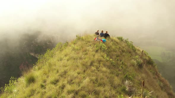 Slowly flying over three backbackers sitting on the edge of a cliff enjoying the stunning view below alt