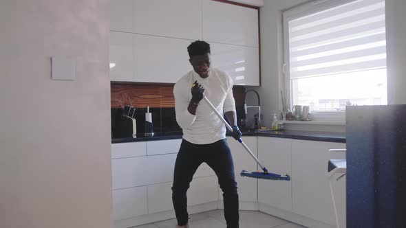 Happy Black Man Having Fun Dancing and Singing While Cleaning Floor in the Kitchen. Domestic Life alt