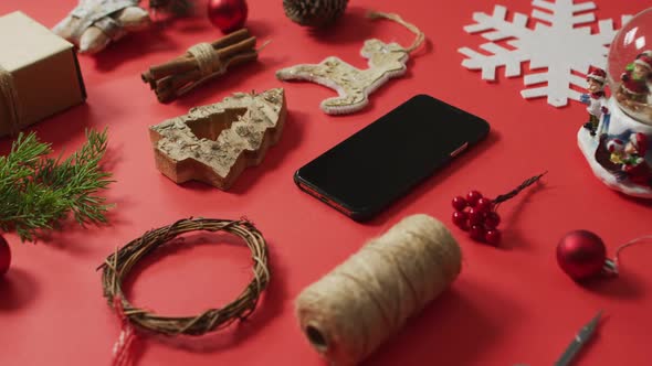 Video of christmas decorations and tree branch with smartphone on red background alt