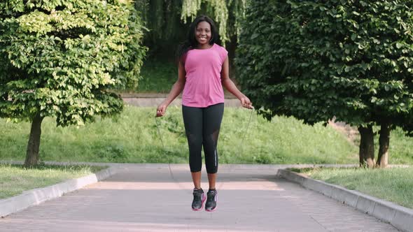 African American Woman Makes a Jump Rope Routine in a City Park alt