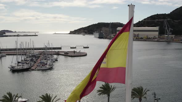 Spanish flag waving in the wind, Cartagena port as background, view from above. Spain