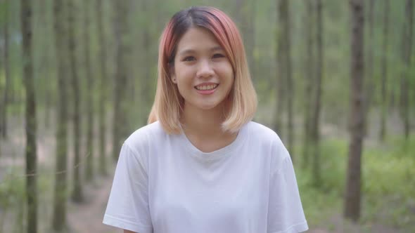 young Asian runner woman feeling happy smiling and looking to camera after running on forest trail. alt
