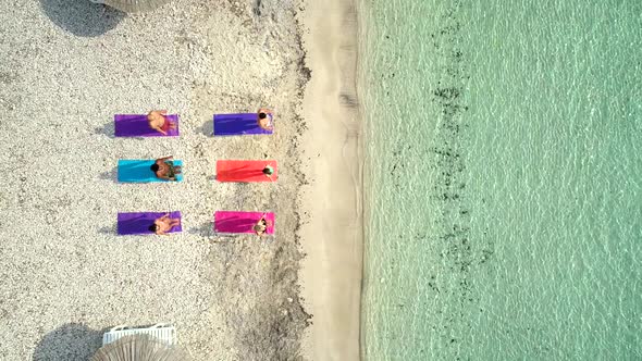Aerial view of group of people doing yoga on colourful mats on the beach. alt