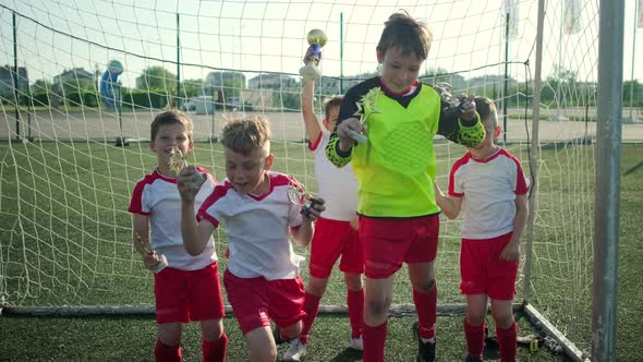 Junior Football Team Jumps Up Holding Trophies alt