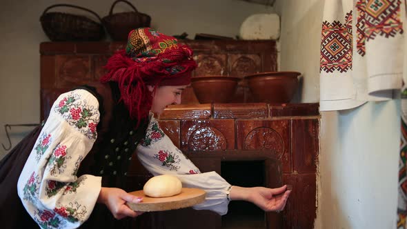 Young Woman in a Traditional Ukrainian Vyshyvanka Costume Puts Raw Bread Dough alt