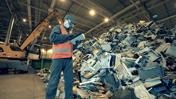 Dumpsite Employee Is Observing a Pile of Broken Electronic Devices. Garbage, Trash, Waste Recycling alt