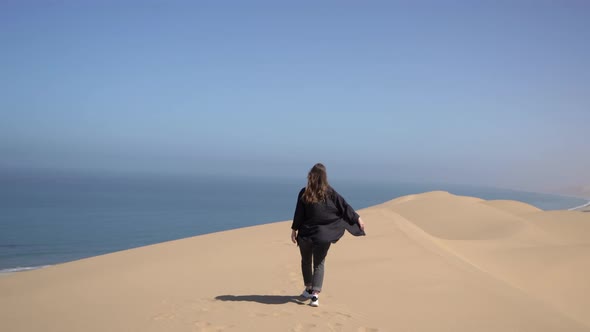 A Young Woman Walks Along Sandy Dunes on Seashore alt
