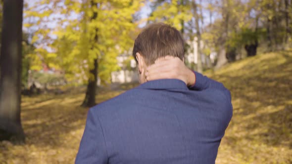 A Middleaged Caucasian Man Walks and Looks Around Then Turns and Smiles at the Camera in a Park