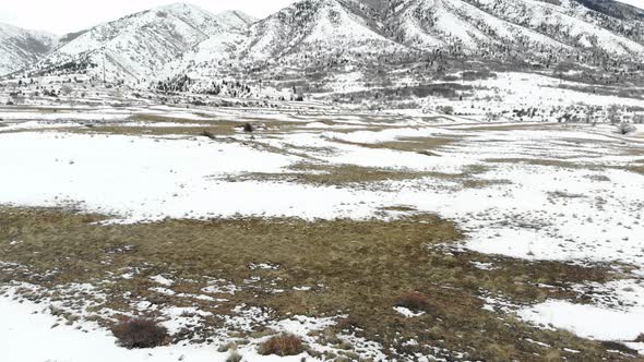 A reveal of a snow covered field at the base of a mountain in winter. alt