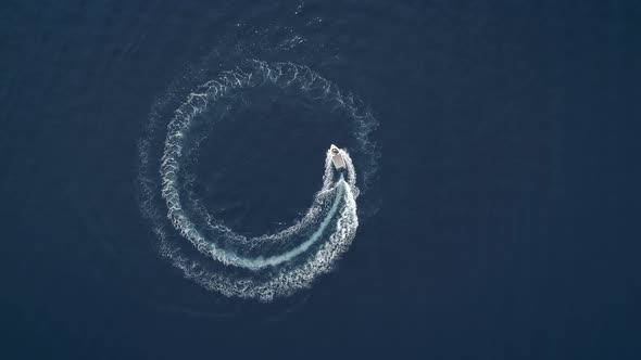 Aerial view of a boat driving in circles forming waves around in Greece. alt