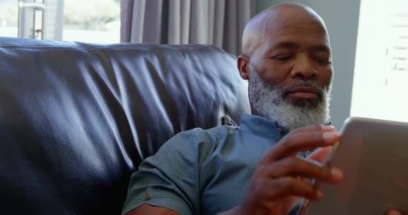 Front view of mature black man using digital tablet in a comfortable home 4k alt