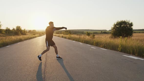Man in Sportswear with Wrapped Hands in Boxing Tapes Training Kicks Outdoors alt