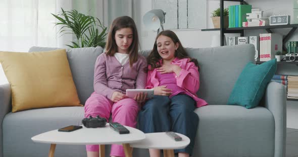 Cute young girls sitting on the sofa and watching videos online together