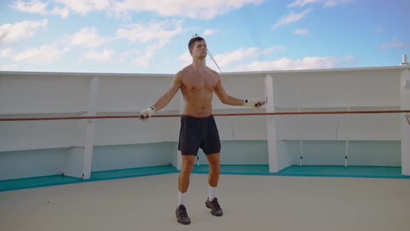Handsome Young Sports Man with Sexy Body and Naked Torso Jumps on Rope Onboard Cruise Ship