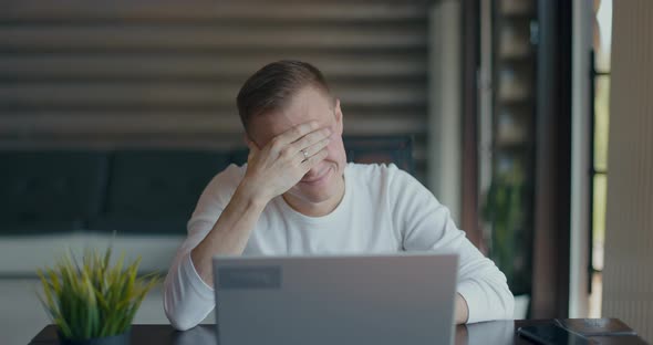 Upset Young Man Covering Face with Palm in Despair After Reading Bad News on Laptop alt
