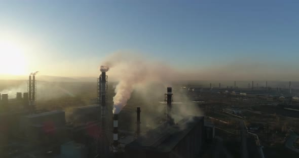 Drone flying over smoking smokestacks of a steel factory. alt