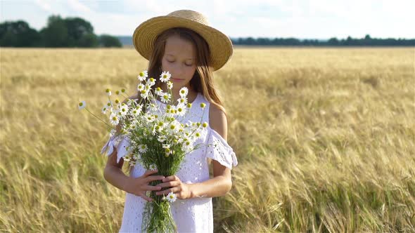 Happy Child in Wheat Field. Beautiful Girl in White Dress in a Straw Hat with Ripe Wheat in Hands